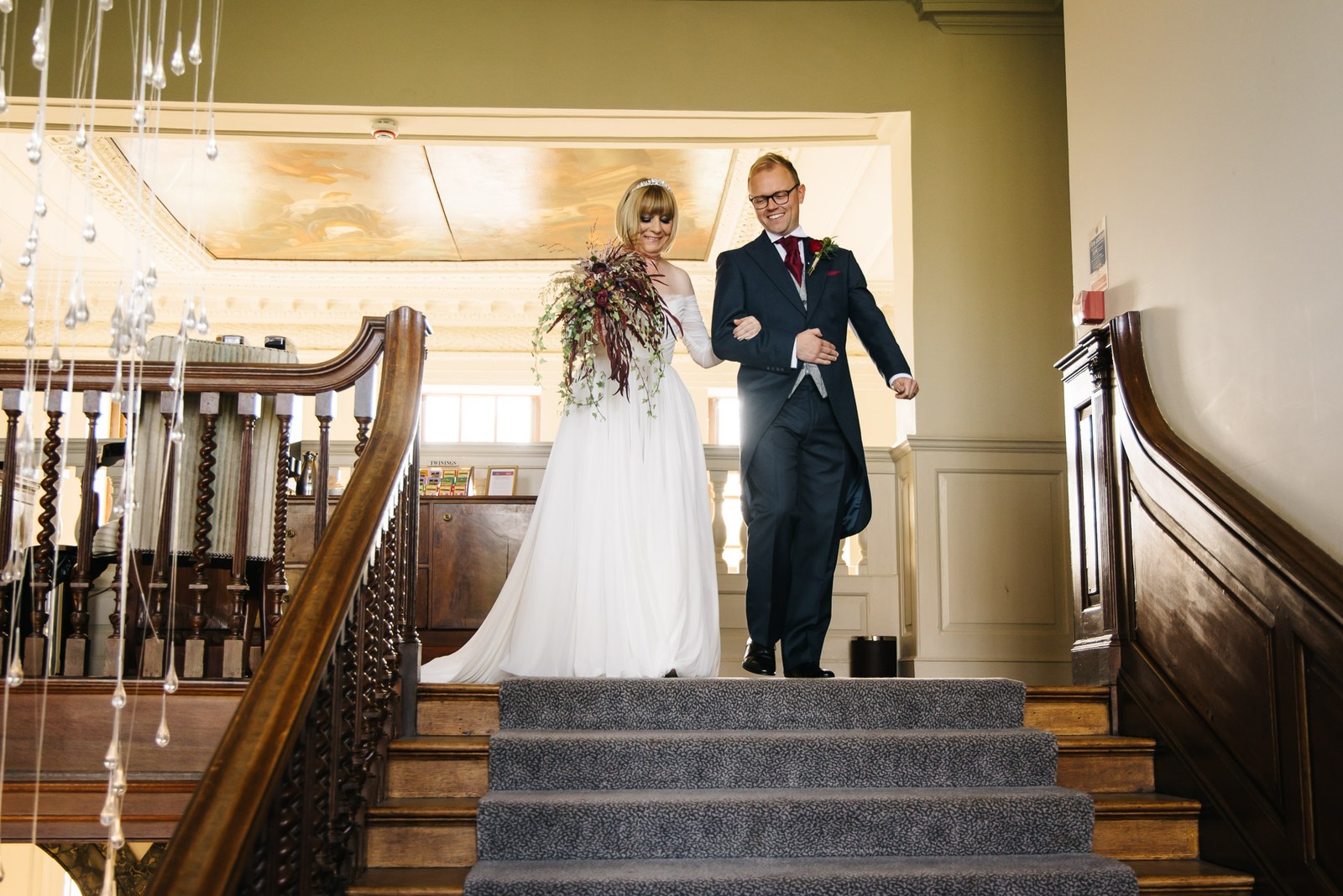 Bride and her escort descending the grand staircase beneath hanging crystals