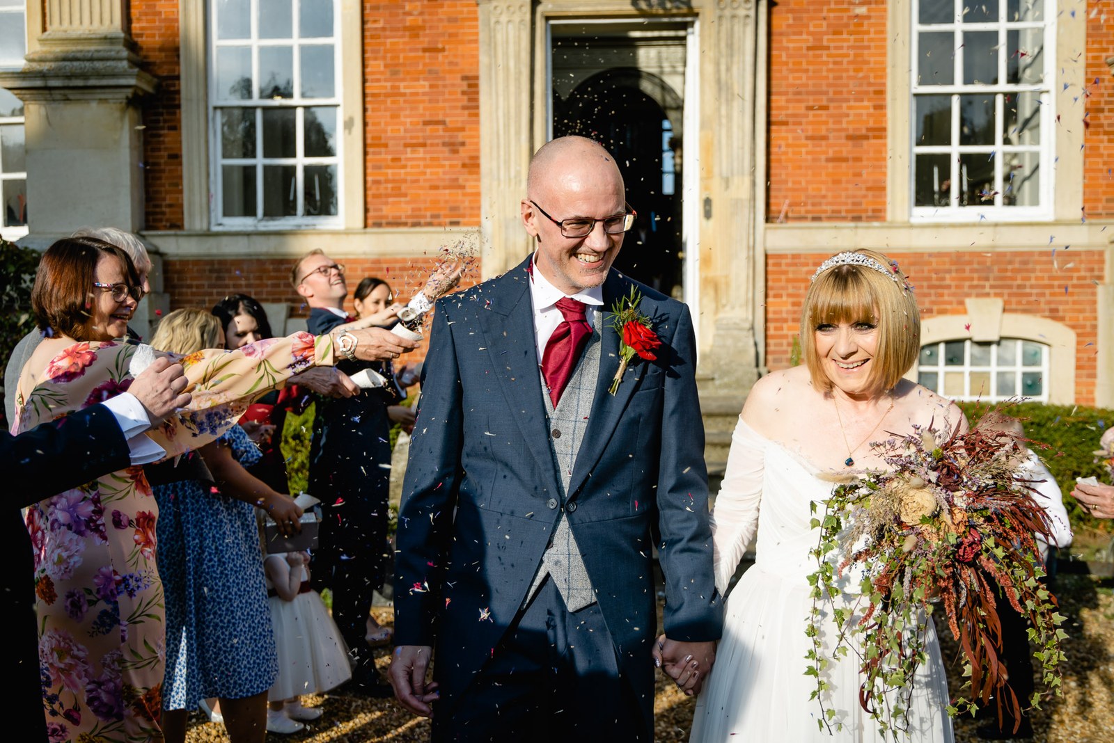 Confetti falls as the couple walk through cheering guests outside Chicheley Hall