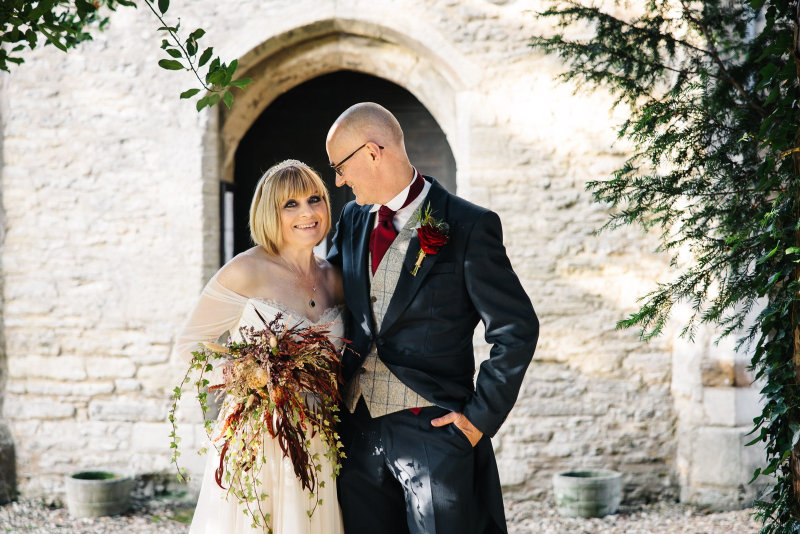 The couple pause before a stone archway, the bride holding a trailing bouquet