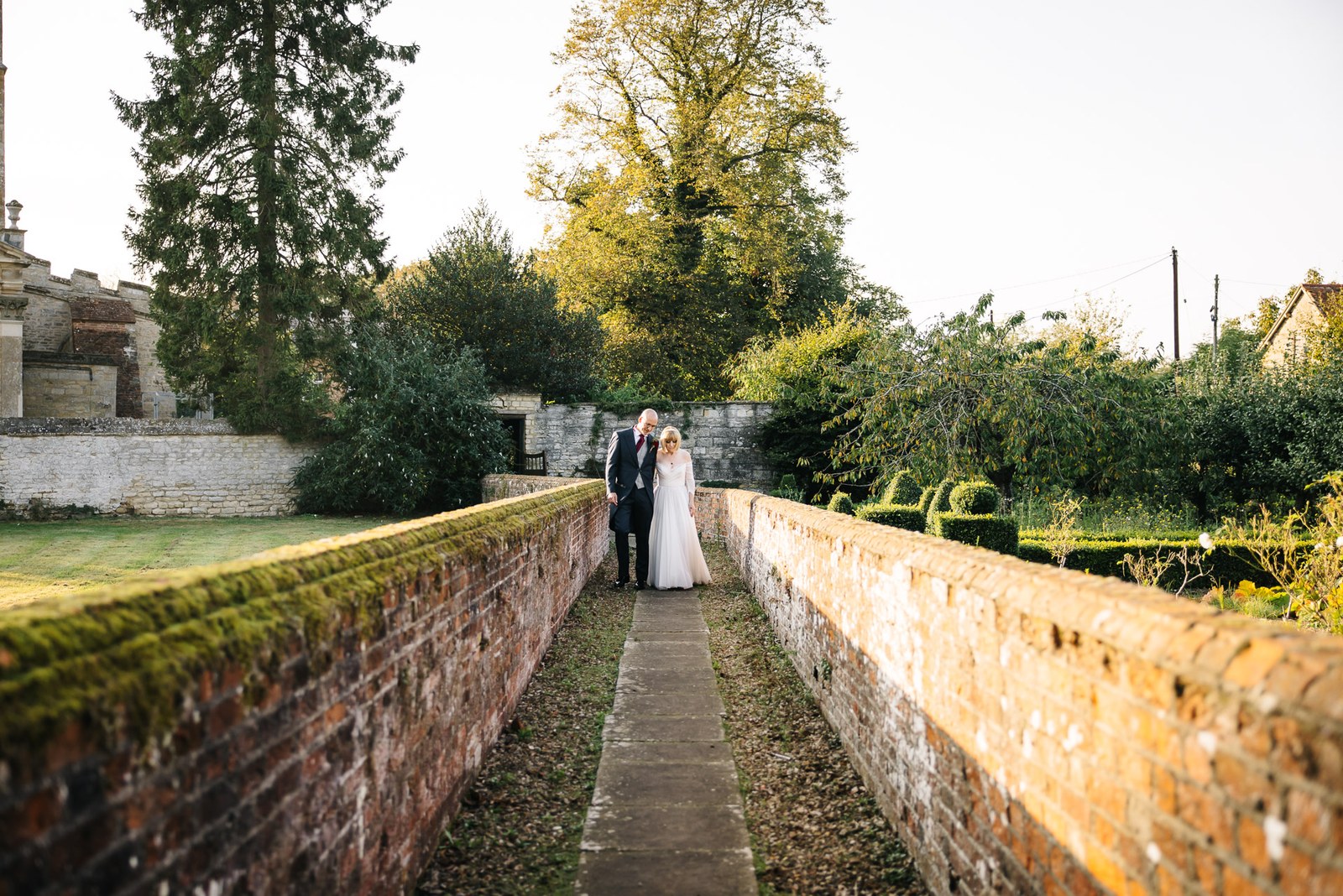 The couple walk a raised brick garden path in the grounds of Chicheley Hall