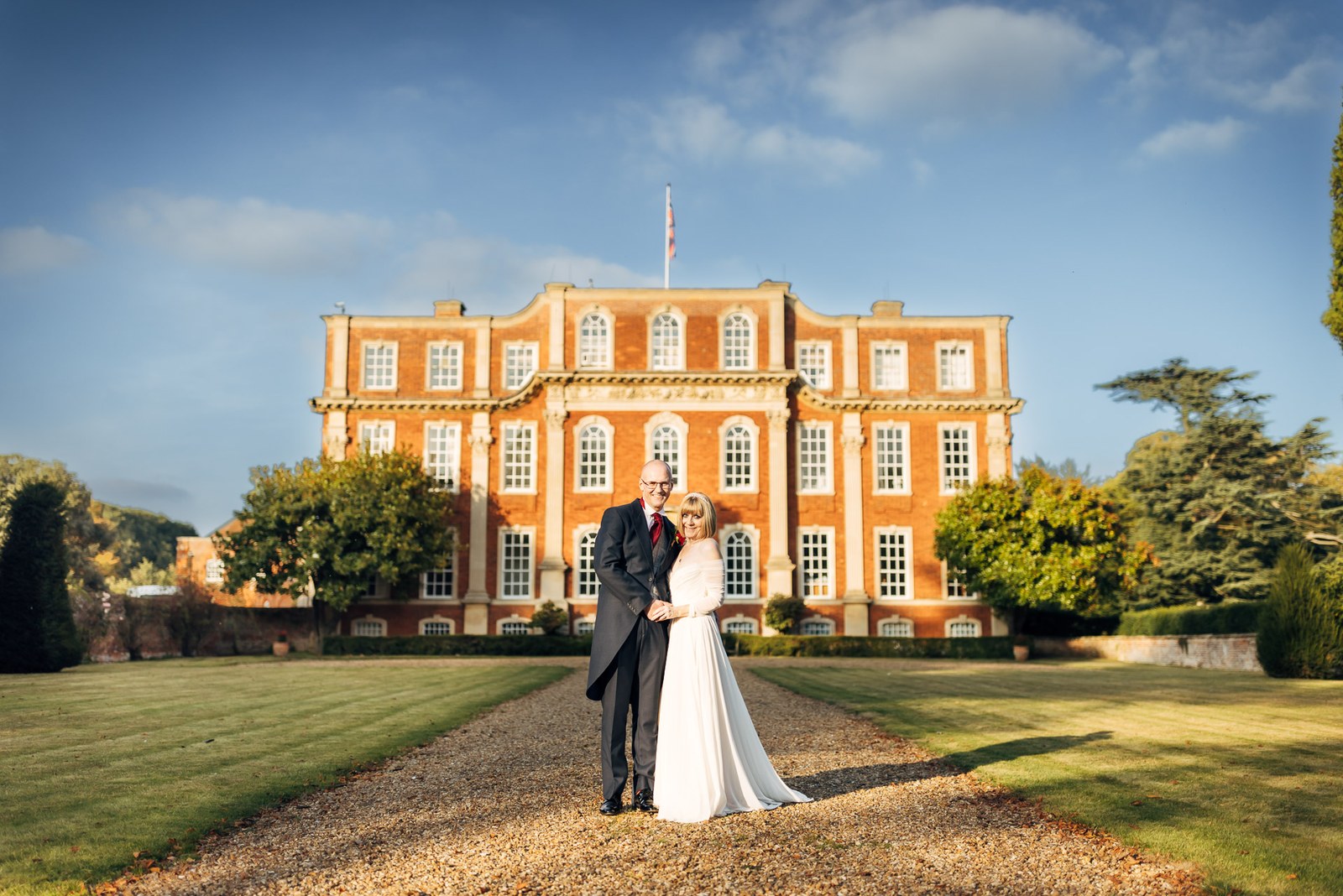 The newlyweds embrace on the drive before the red-brick facade of Chicheley Hall