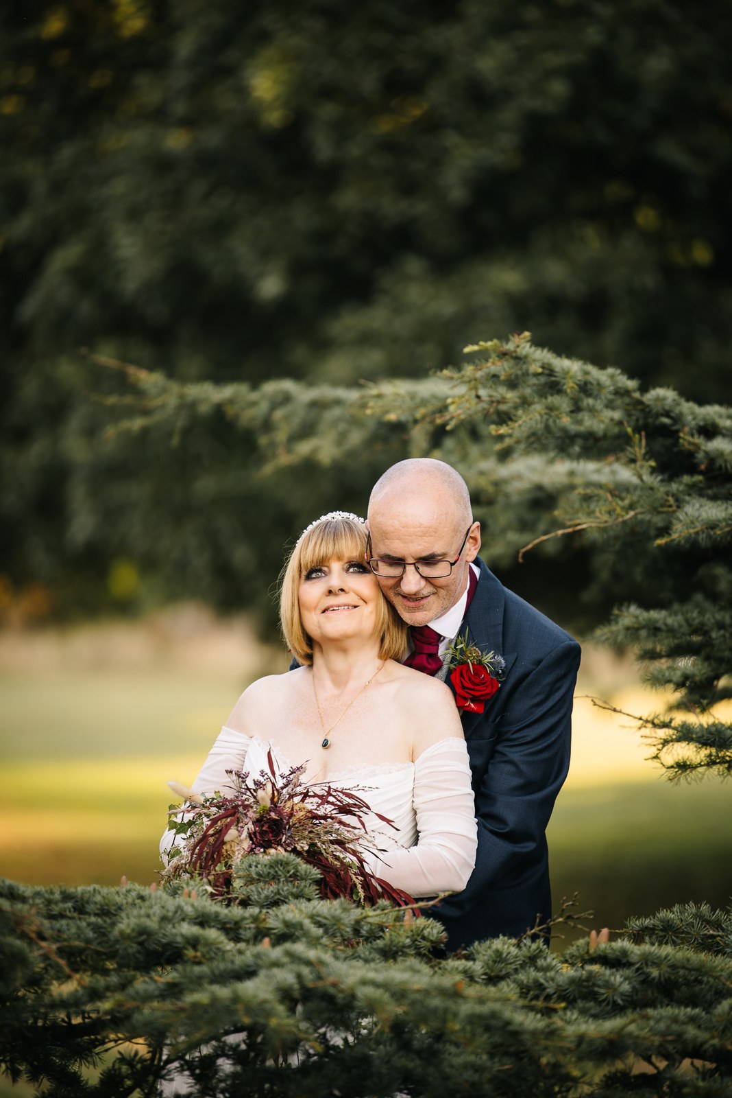 Portrait of the couple embracing against soft evergreen foliage
