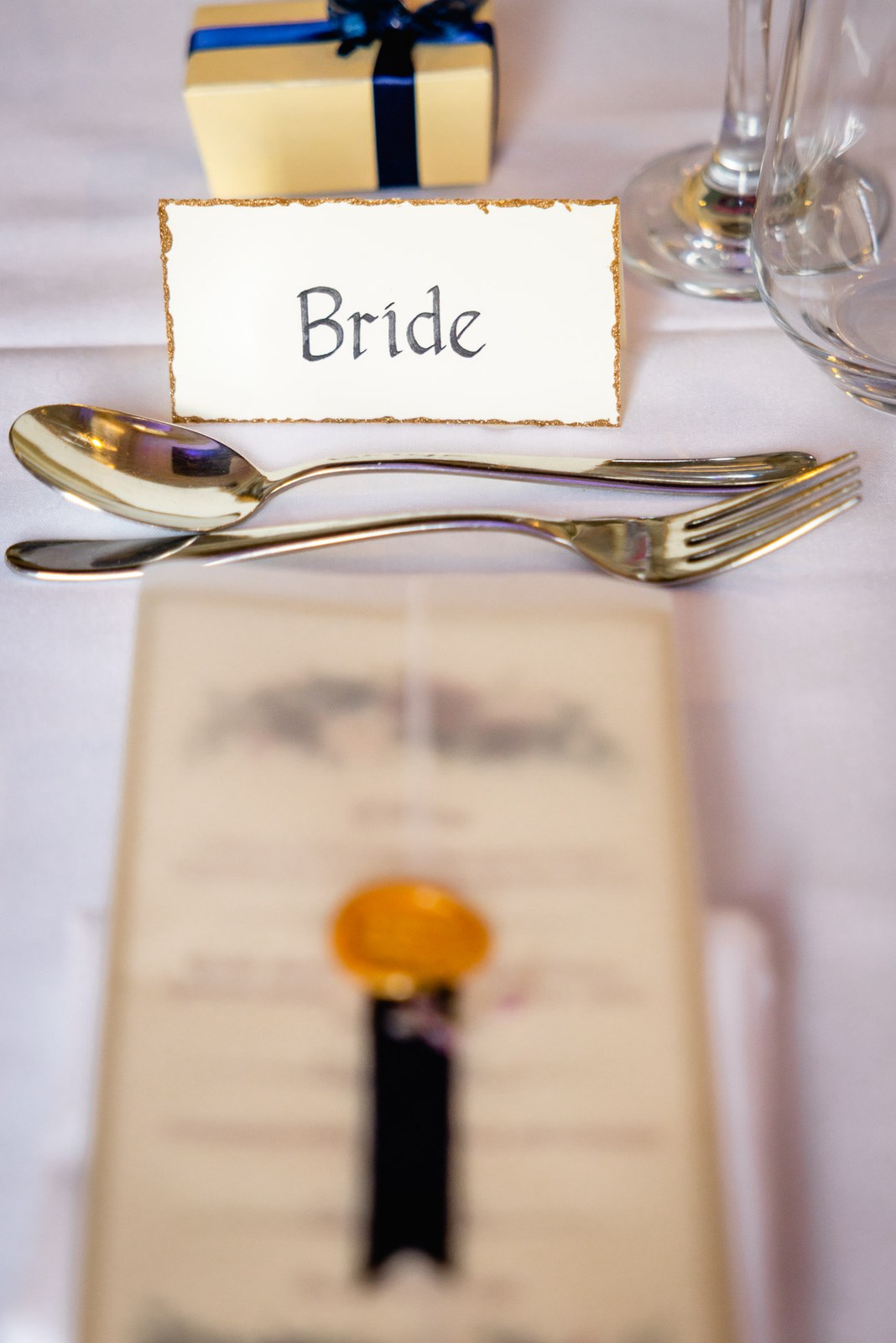 A 'Bride' place card with gold cutlery and a menu on the top table