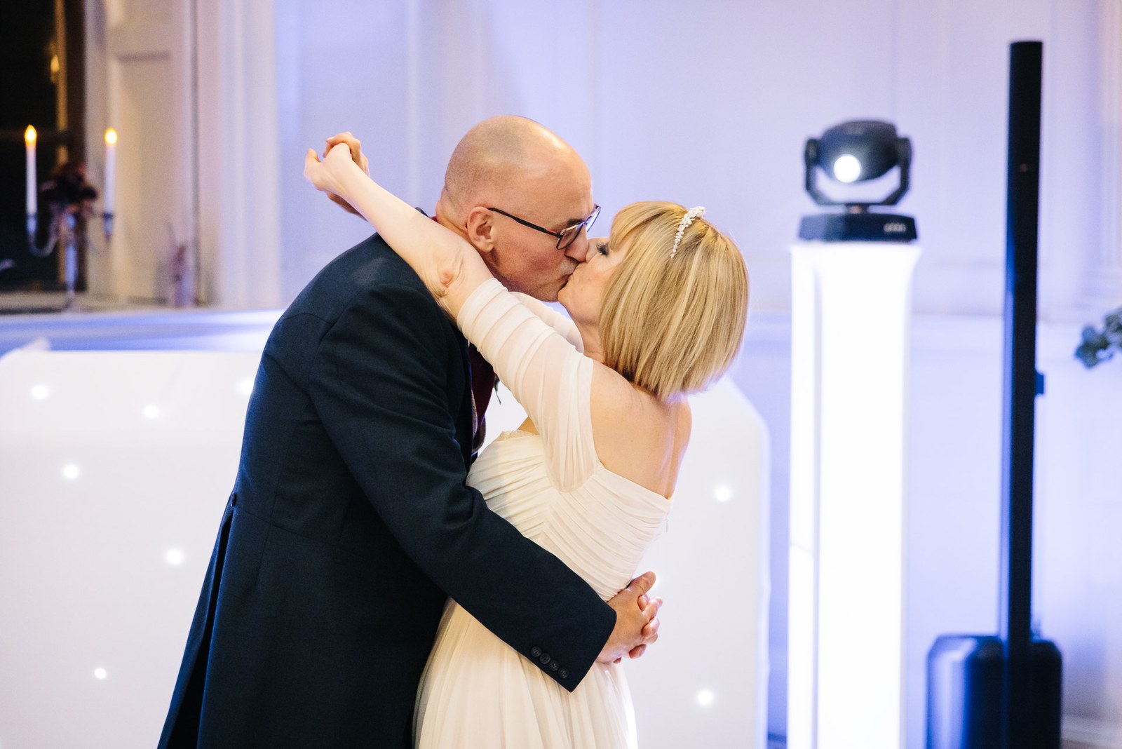 The newlyweds kiss during their first dance beside a lit DJ booth