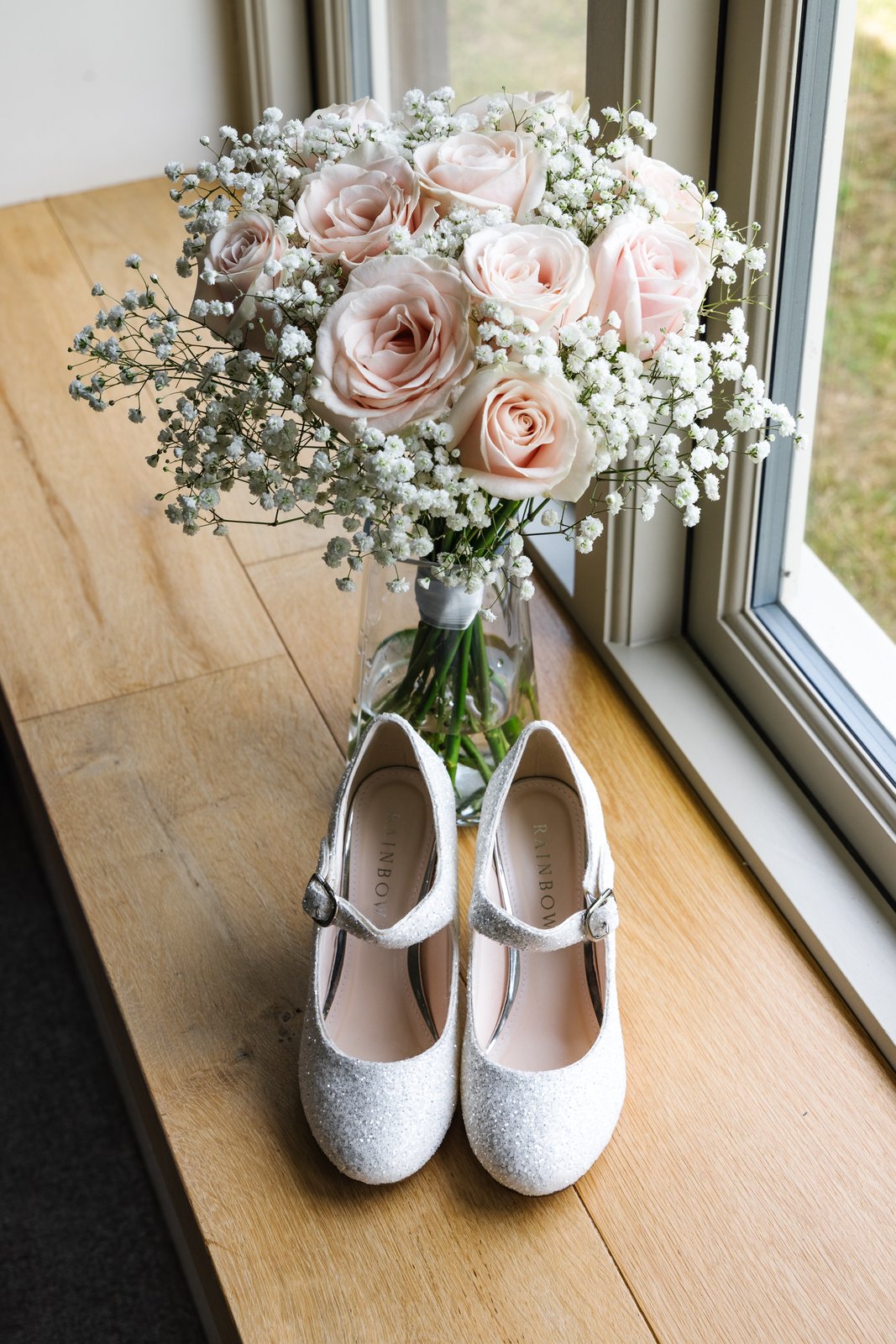 The bridal bouquet on a windowsill with the bride's shoes on the floor below