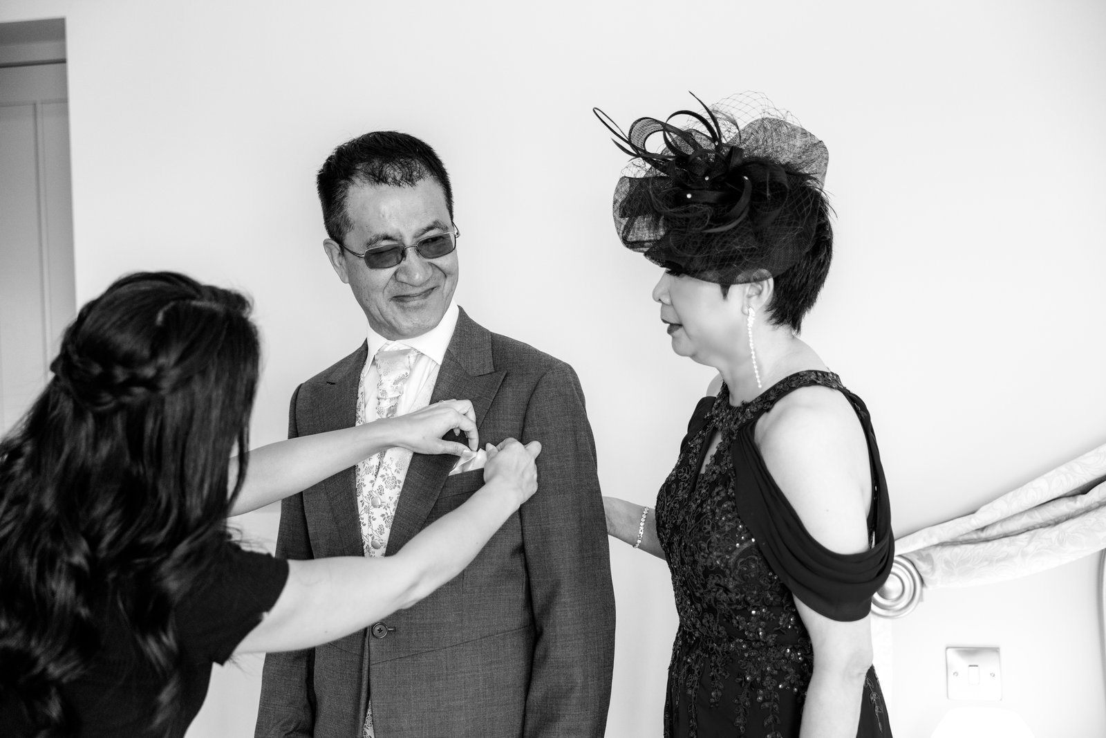 Black and white frame of a buttonhole being pinned to the bride's father's suit