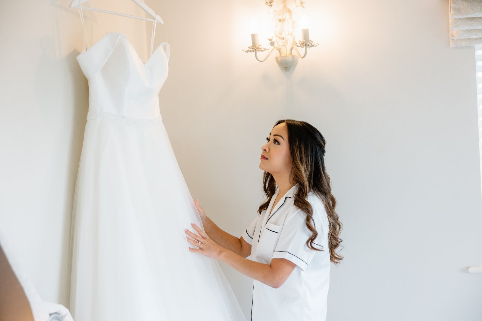 The bride reaching up to her dress on its hanger before getting changed
