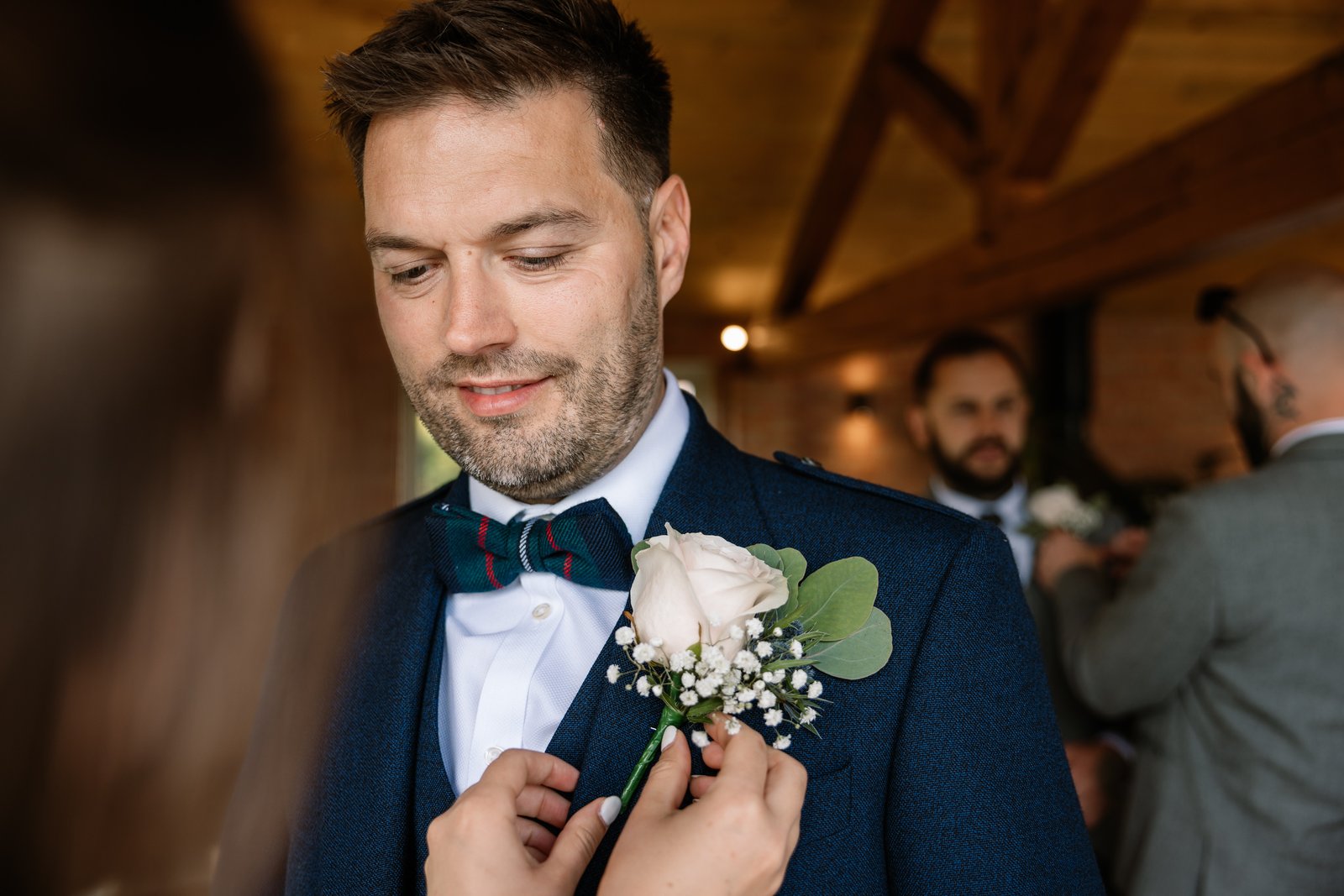 A buttonhole being pinned to the groom's navy jacket before the ceremony