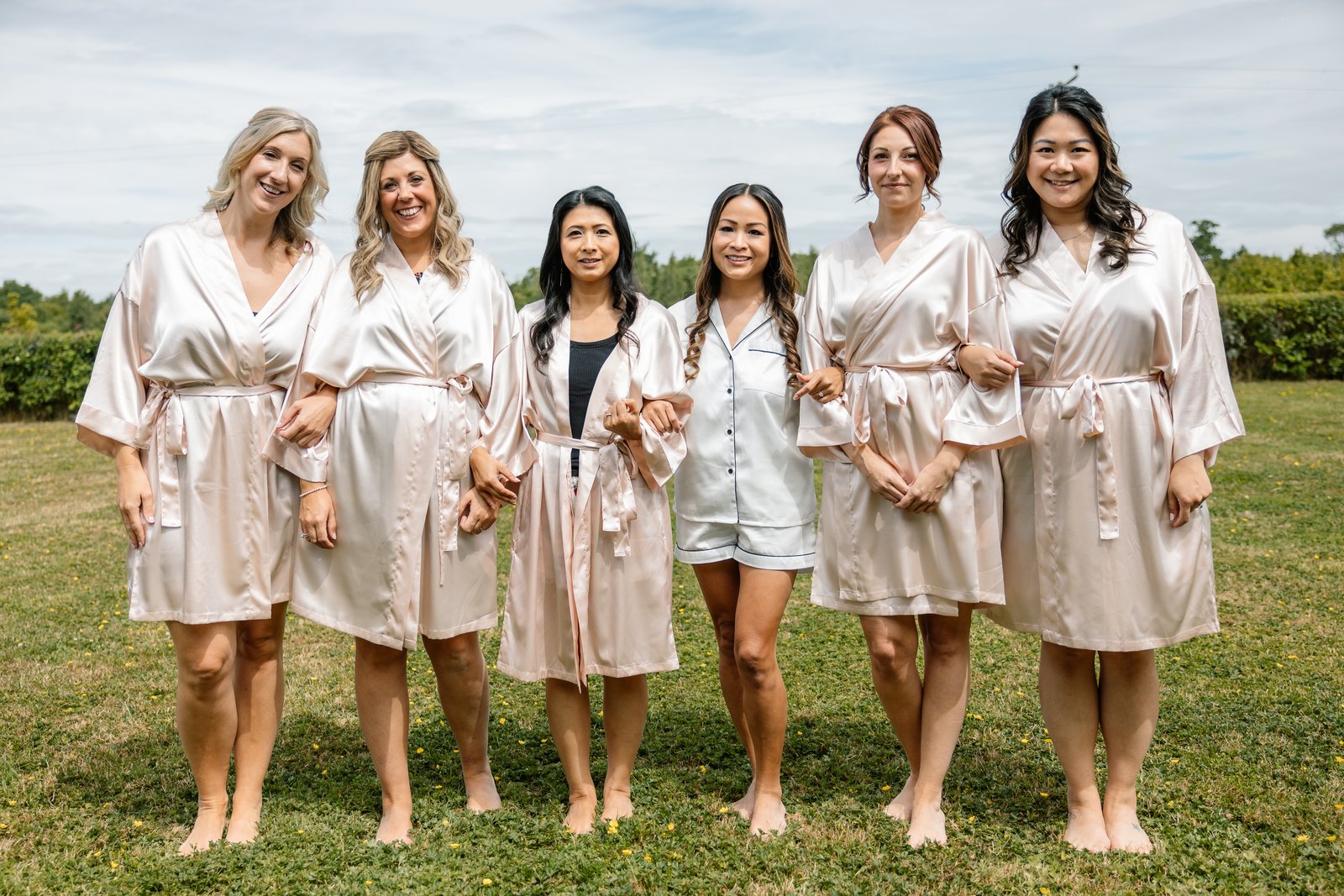The bride and her bridesmaids in matching robes standing barefoot on the lawn