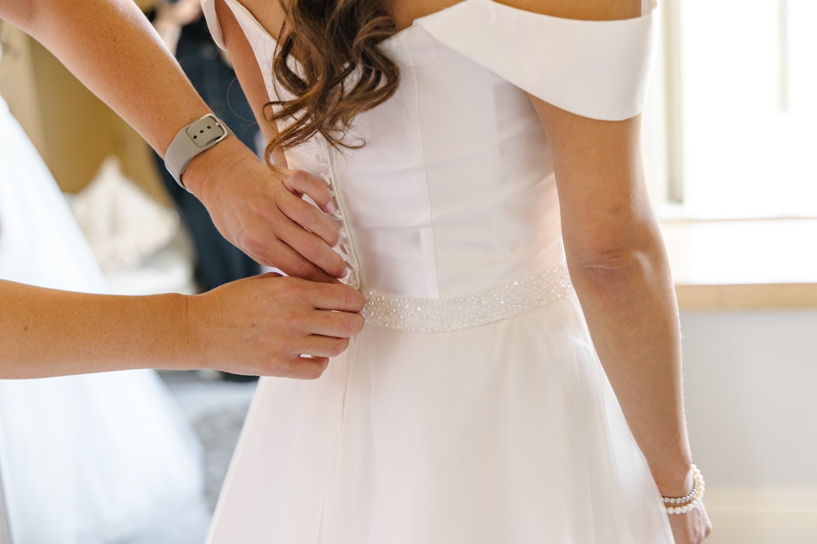 Close view of hands fastening the back of the bride's dress