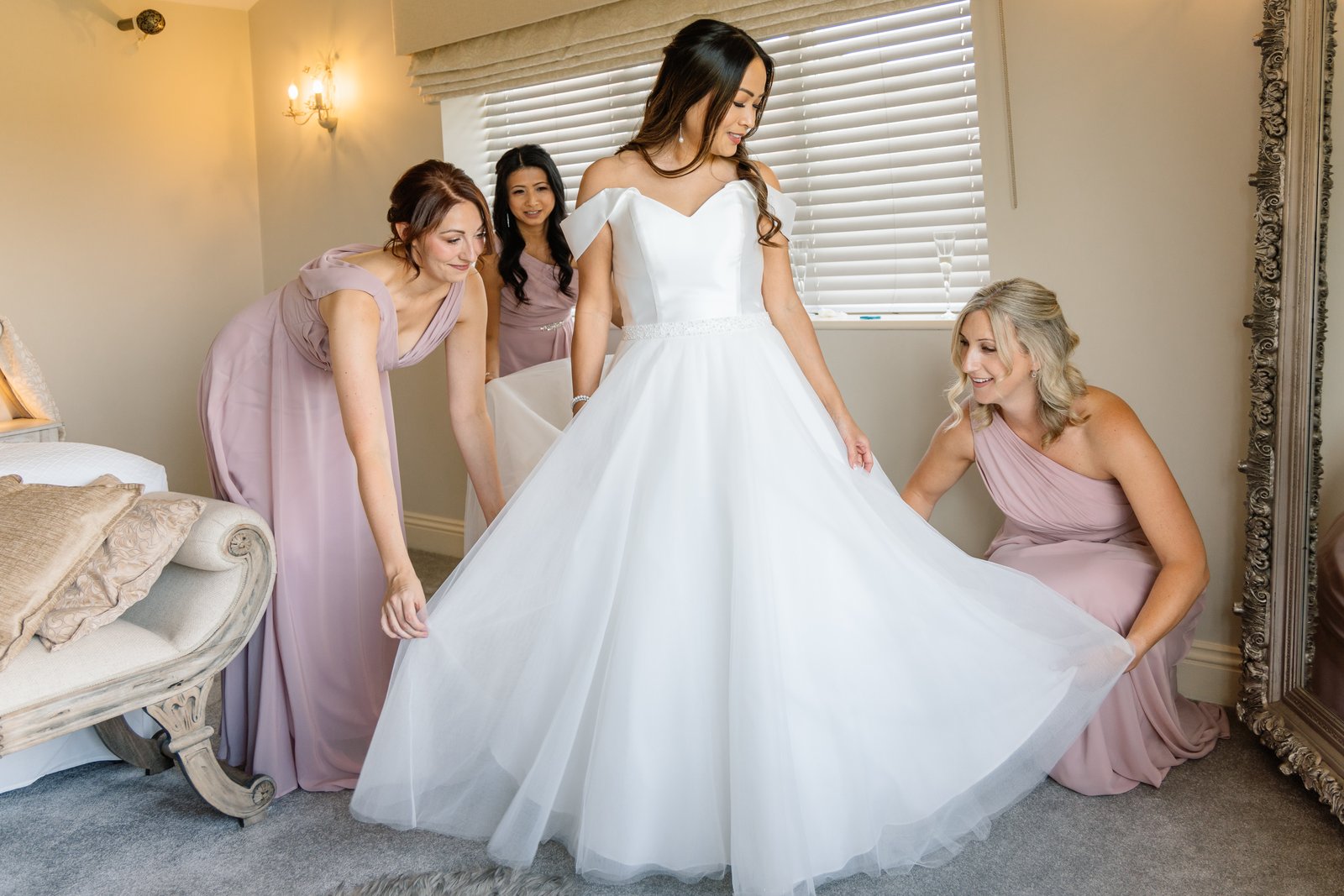 Bridesmaids helping the bride into her dress beside a tall mirror