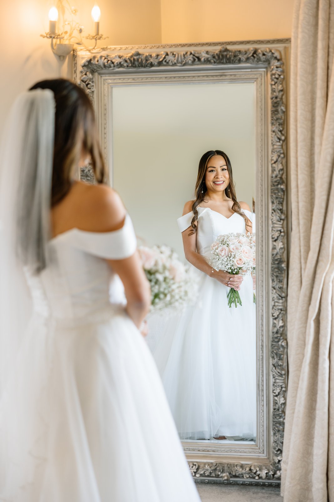 The bride reflected in an ornate mirror with her veil down her back