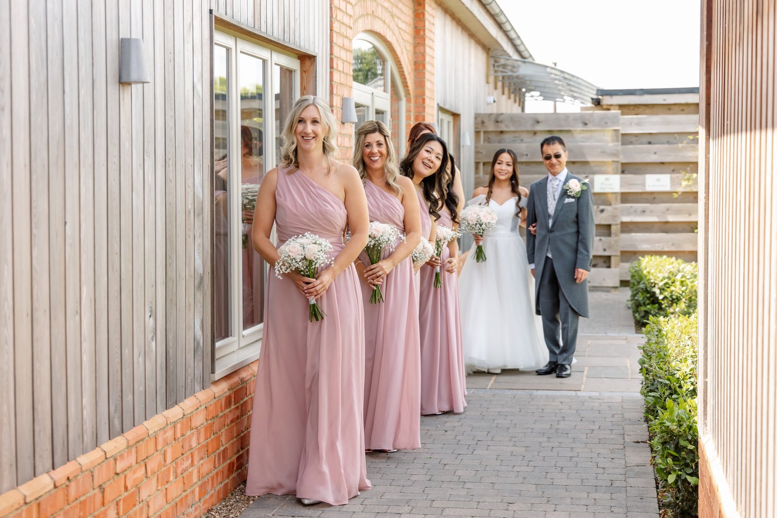 Bridesmaids waiting on the paved path alongside the buildings at Cider Mill Barns