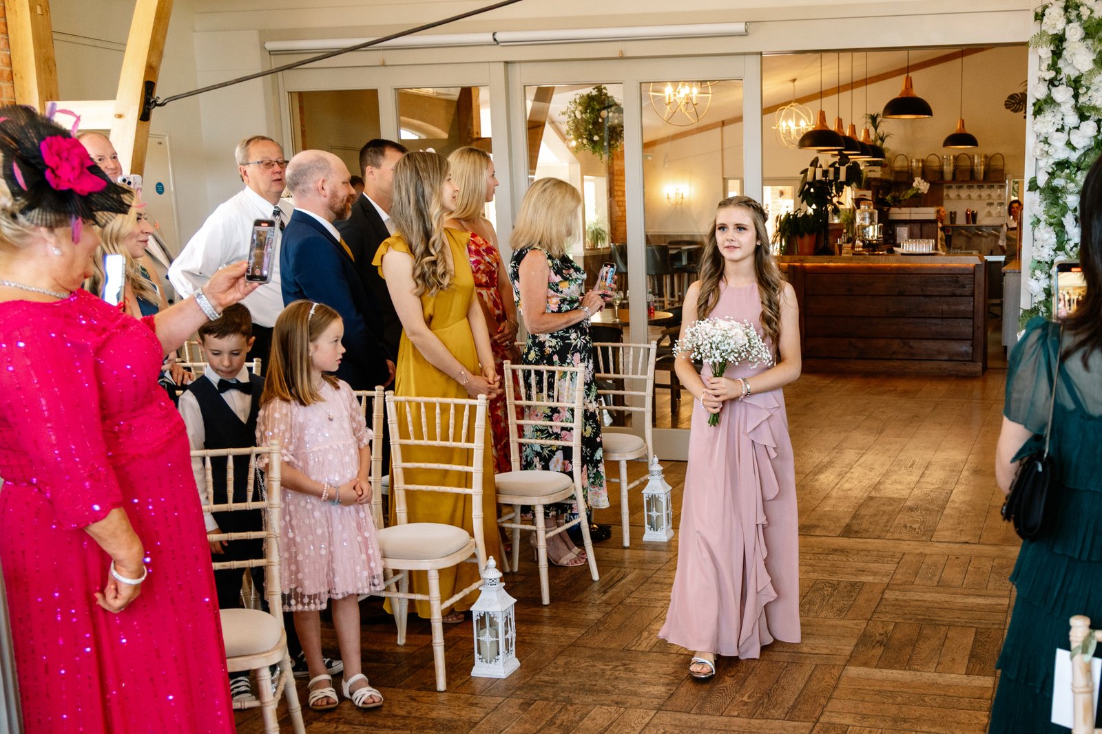 A bridesmaid walking in as guests turn to watch, the bar behind her