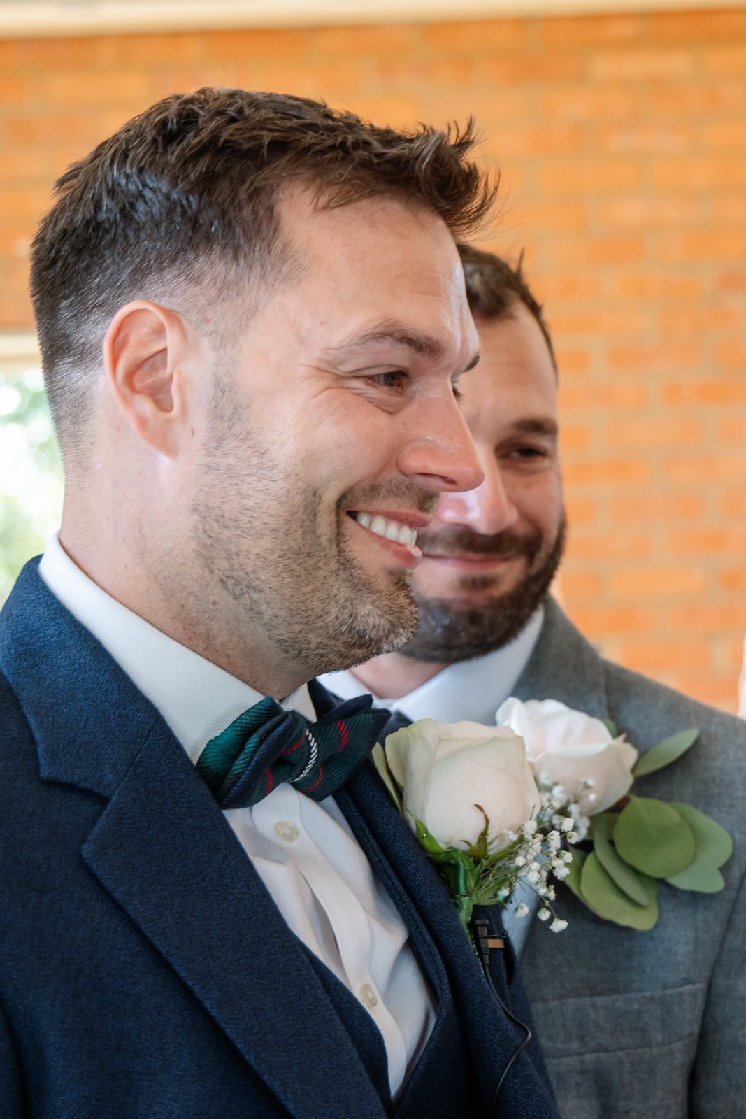 The groom watching the bride come in, a groomsman smiling behind him
