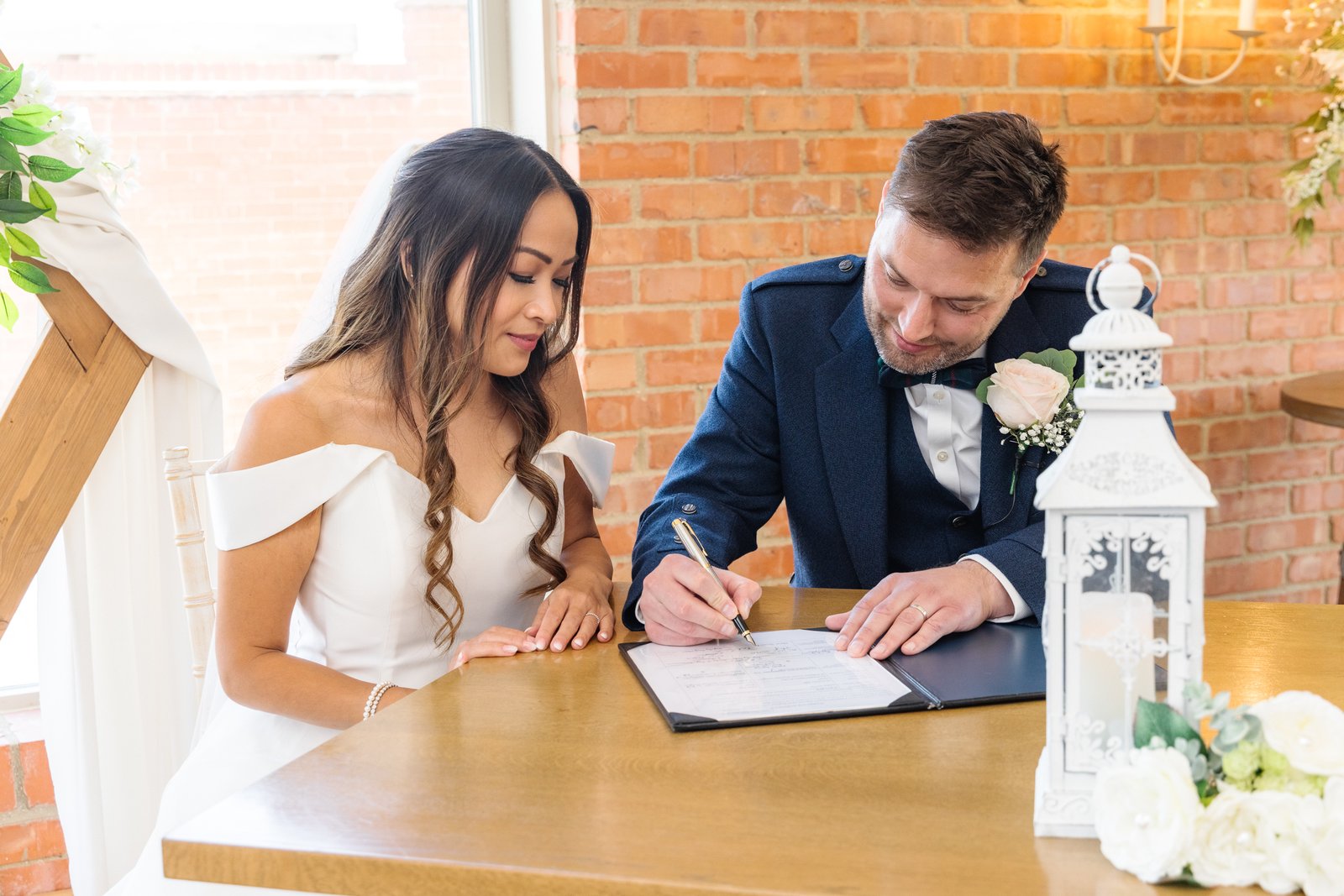 The couple signing the register at a table against the brick wall