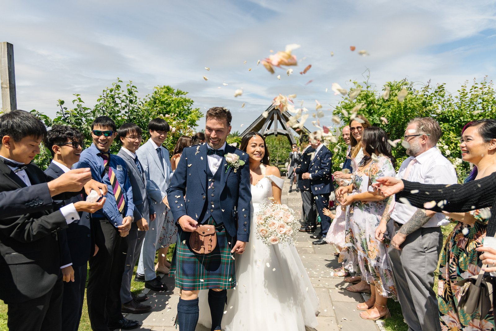 Guests throwing confetti over the couple on the path between the rows at Cider Mill Barns