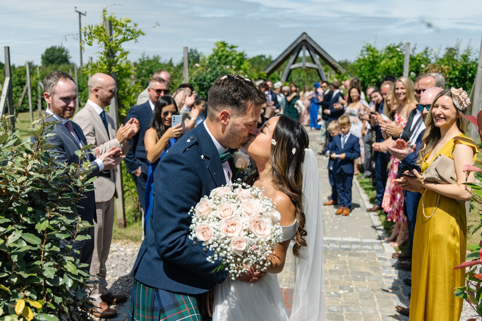 The couple kissing halfway down the confetti line with guests either side