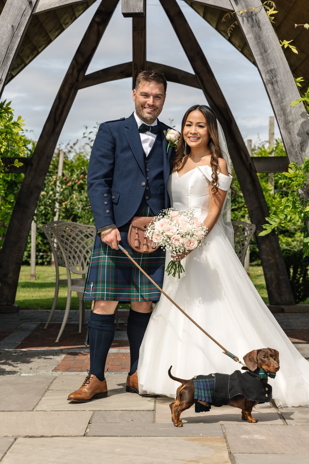 The couple with a dachshund on a lead under the oak frame at Cider Mill Barns