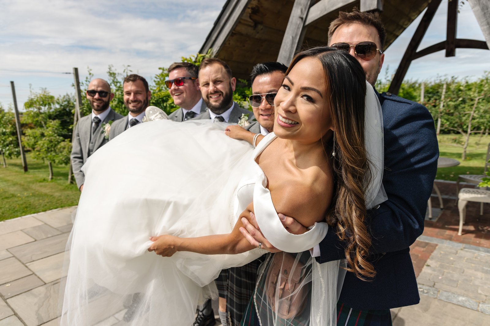 The groom carrying the bride past the groomsmen on the terrace