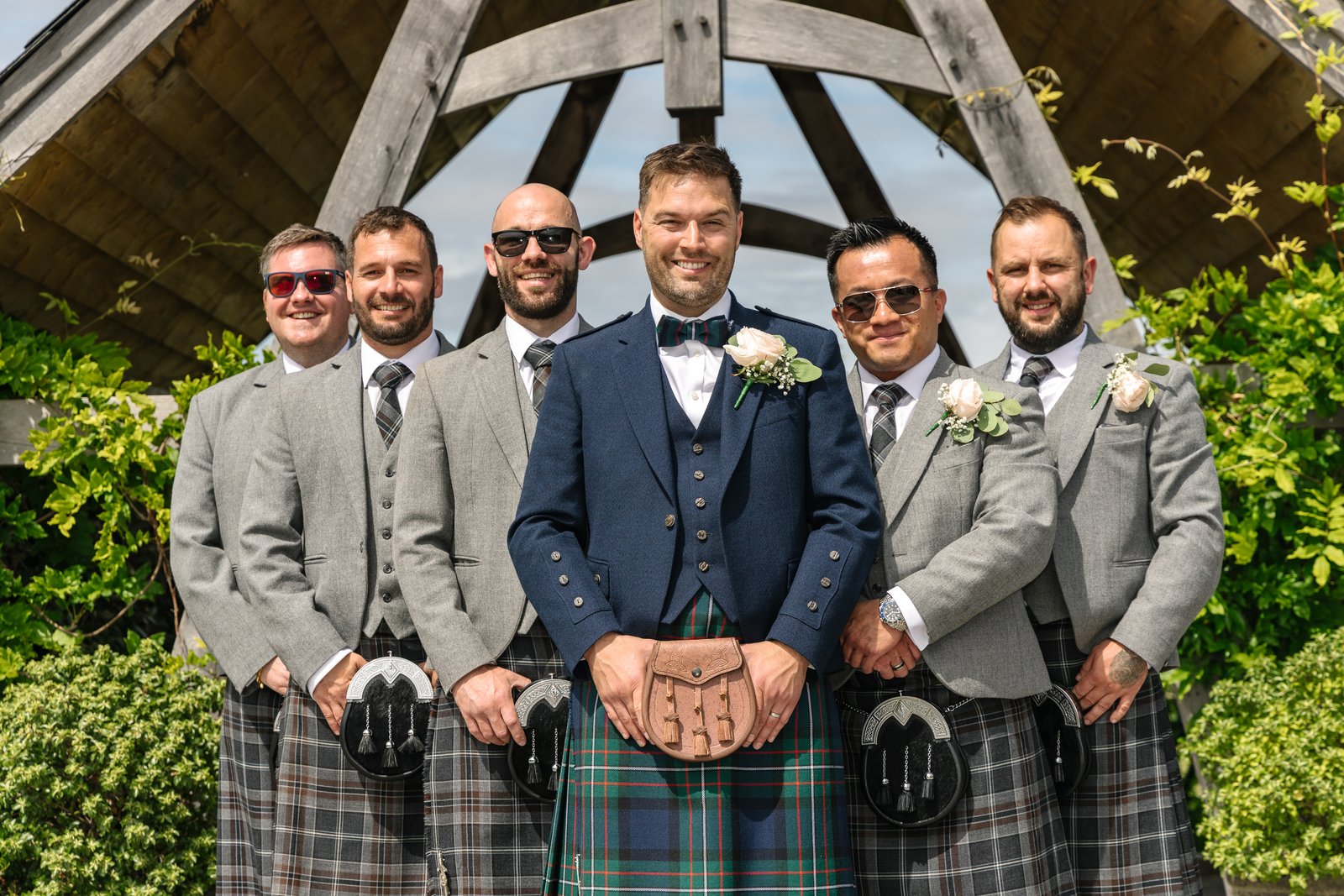 The groom and his groomsmen in kilts under the oak frame at Cider Mill Barns