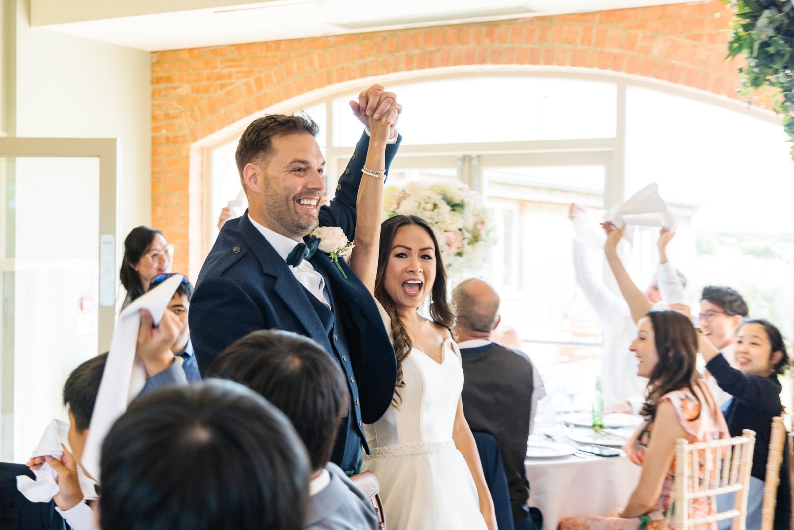 The couple cheering at their table as guests wave napkins over their heads