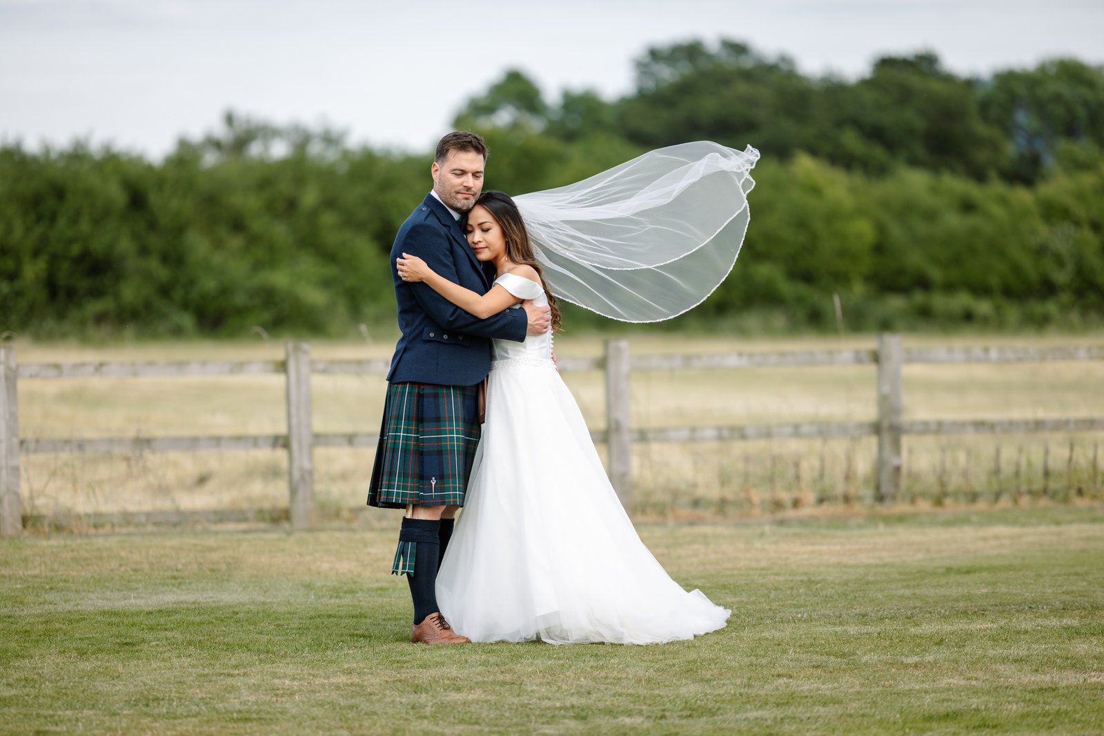 The couple holding each other in a field beside Cider Mill Barns, the veil lifting in the wind