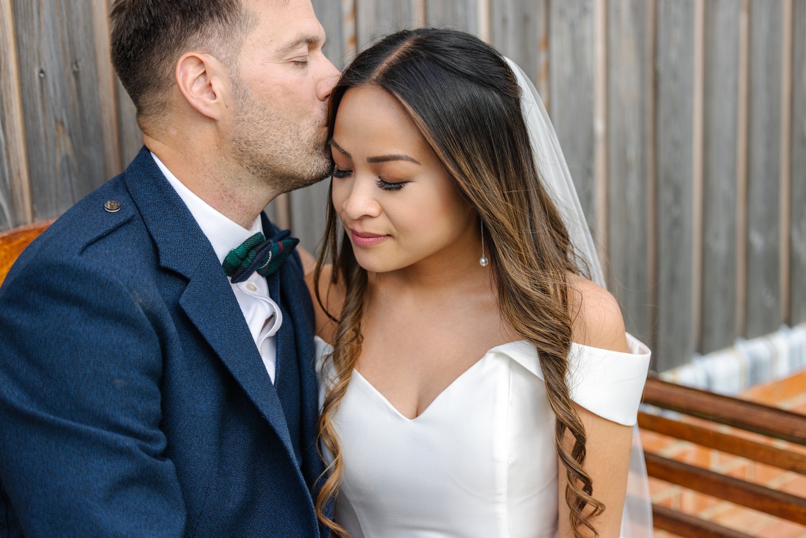 The groom kissing the bride on the side of her head