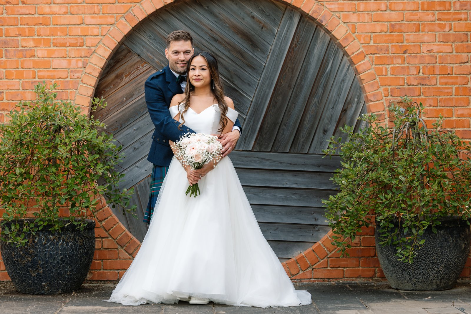 The couple framed in the round wooden door set into the brick wall at Cider Mill Barns
