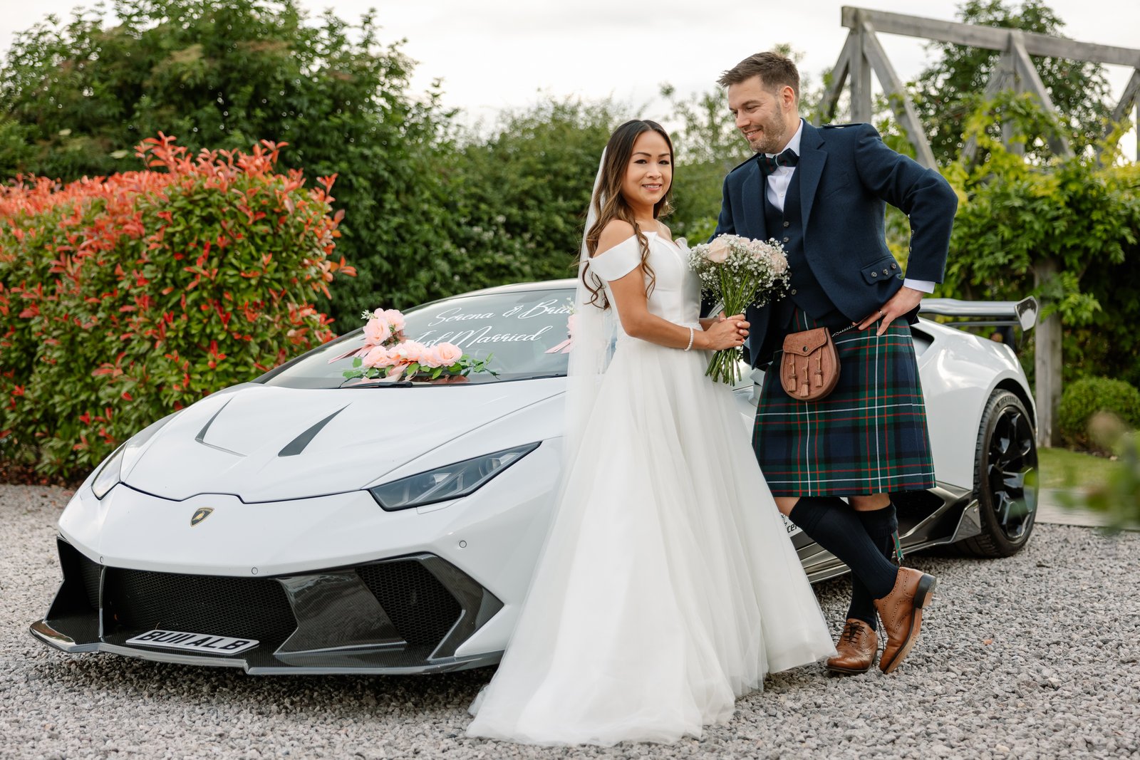 The couple standing beside a white sports car on the gravel drive