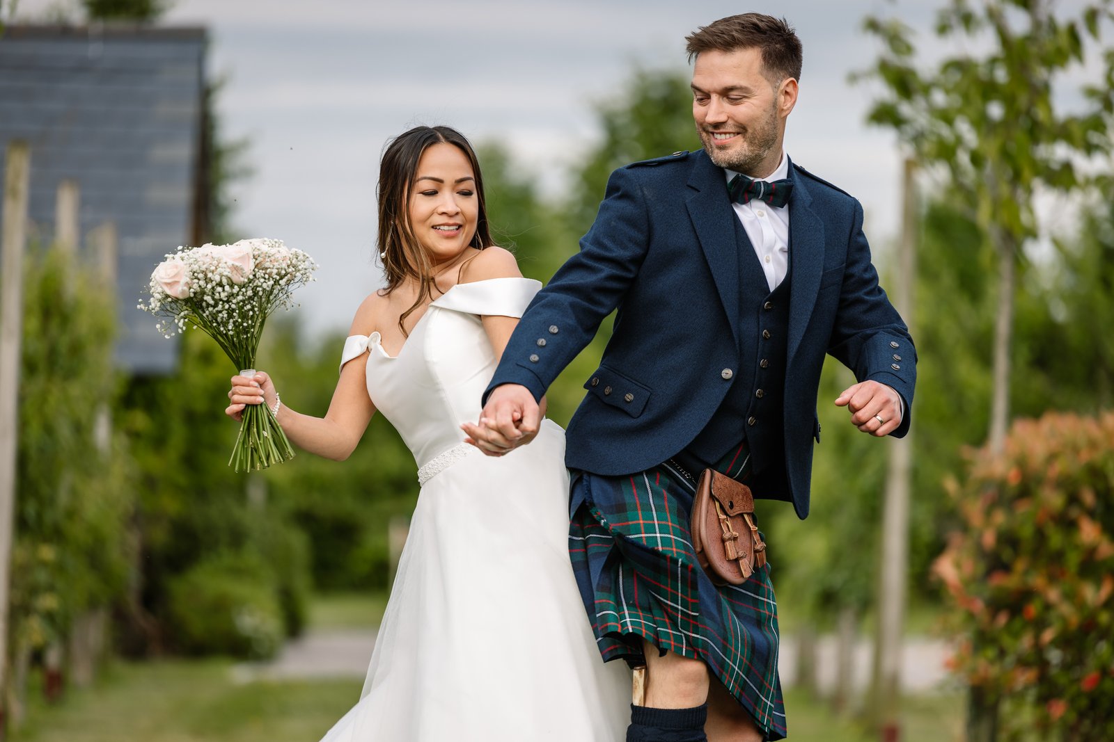 The couple walking through the garden, the bride holding her bouquet out