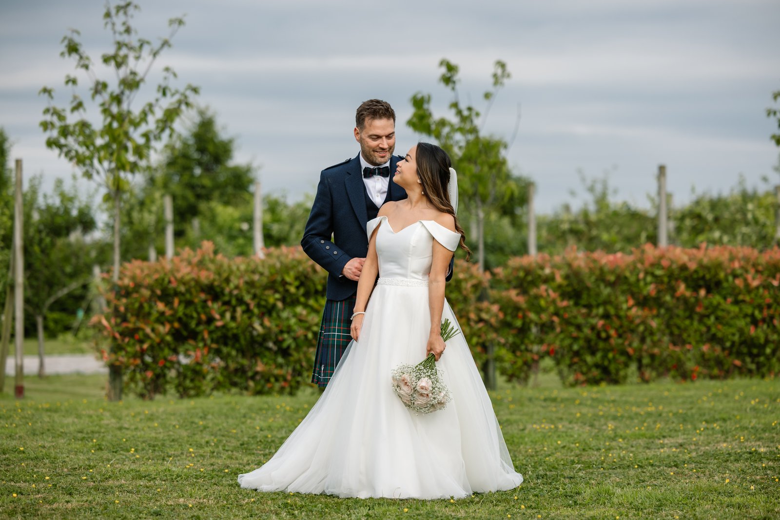 The couple standing on the grass among the rows at Cider Mill Barns
