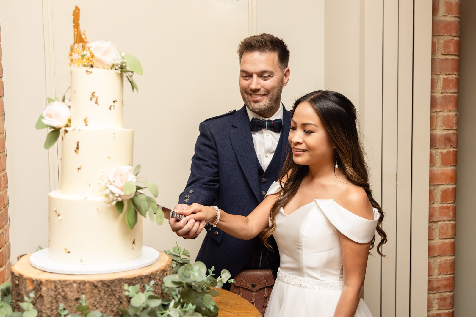 The couple cutting a tall iced wedding cake decorated with roses