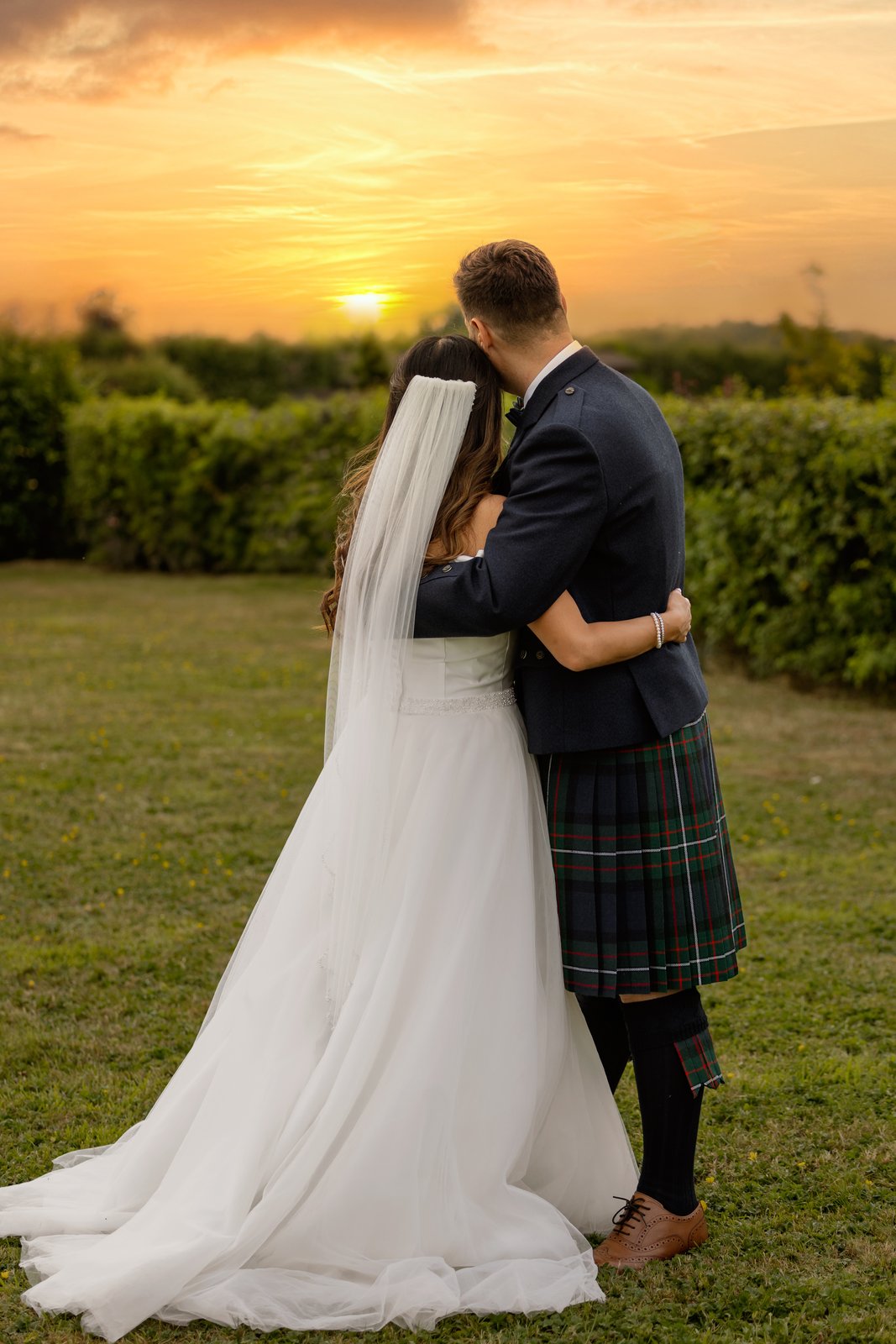 The couple holding each other in a field at sunset beside Cider Mill Barns