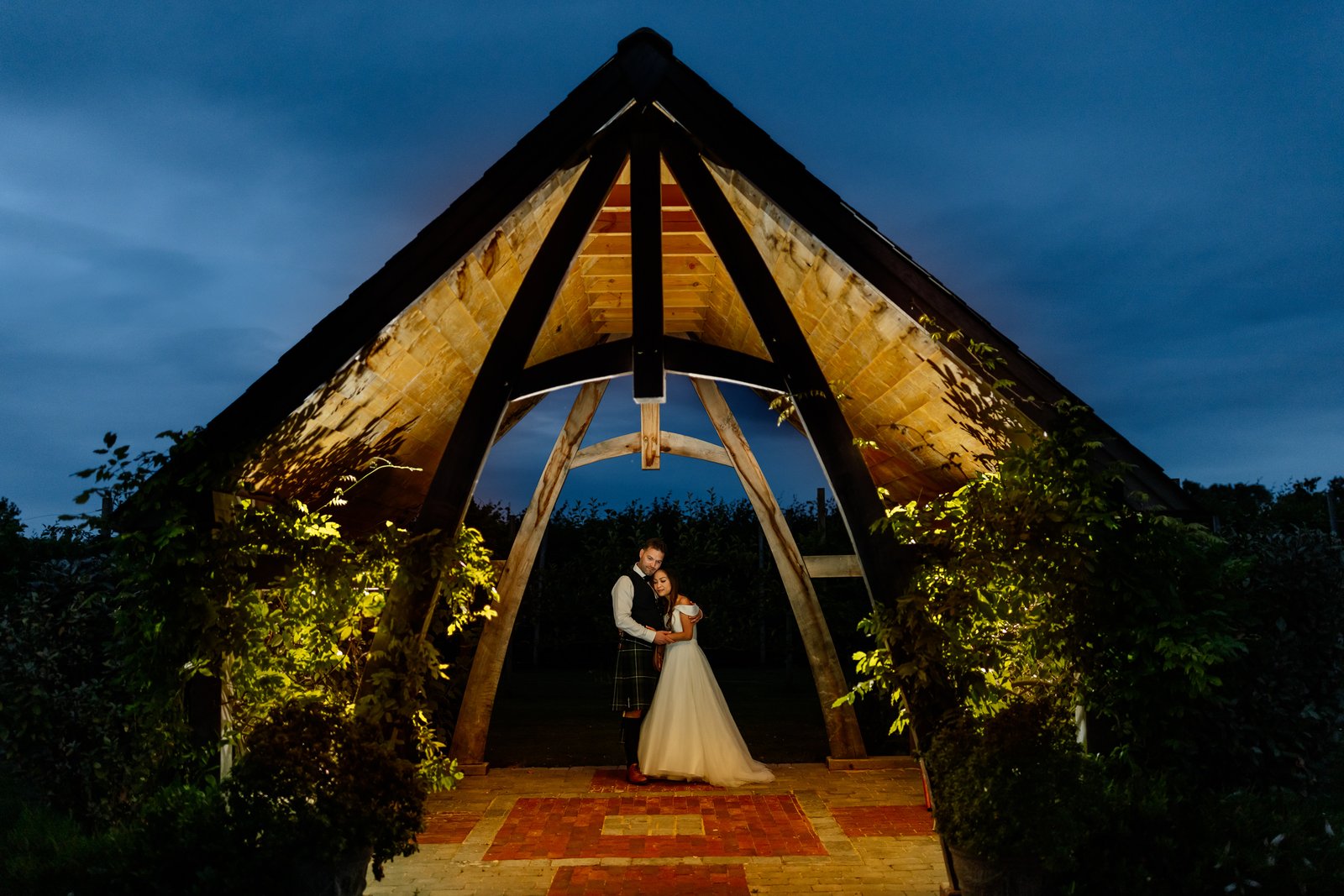 The couple under the lit oak frame at Cider Mill Barns after dark