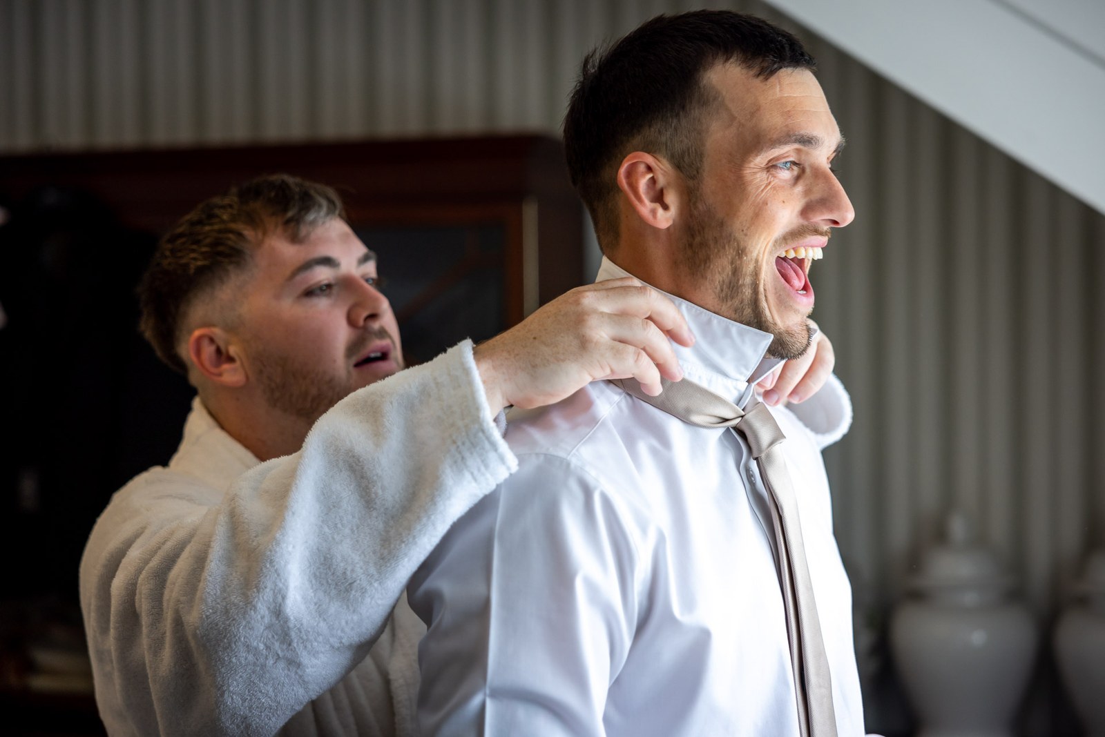 The groom laughs as a helper adjusts his collar and tie