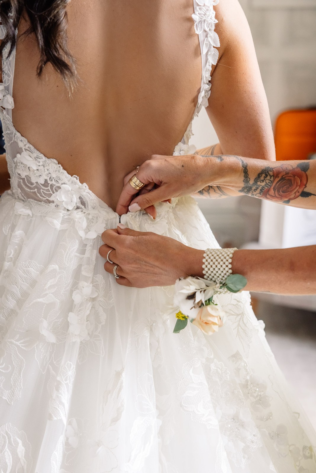 A helper fastens the back of the bride's lace gown