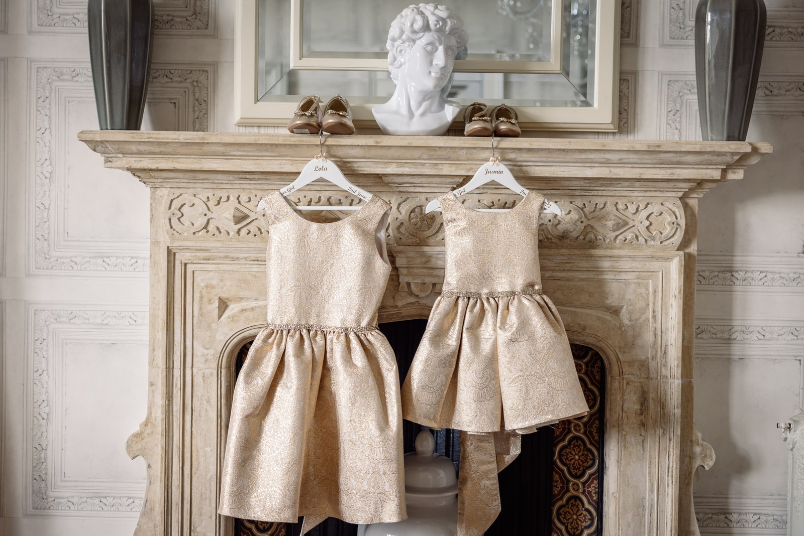 Two flower girls' dresses hung on the carved stone fireplace at Clevedon Hall beneath a marble bust