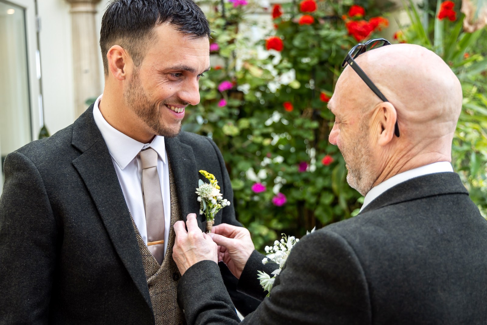 An older man pins a buttonhole to the groom's lapel in the garden