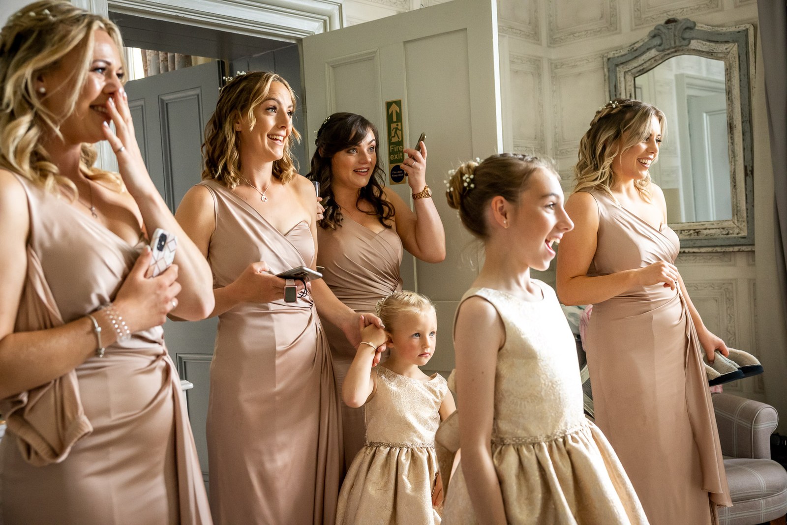 Bridesmaids in blush satin gowns getting ready with the flower girls