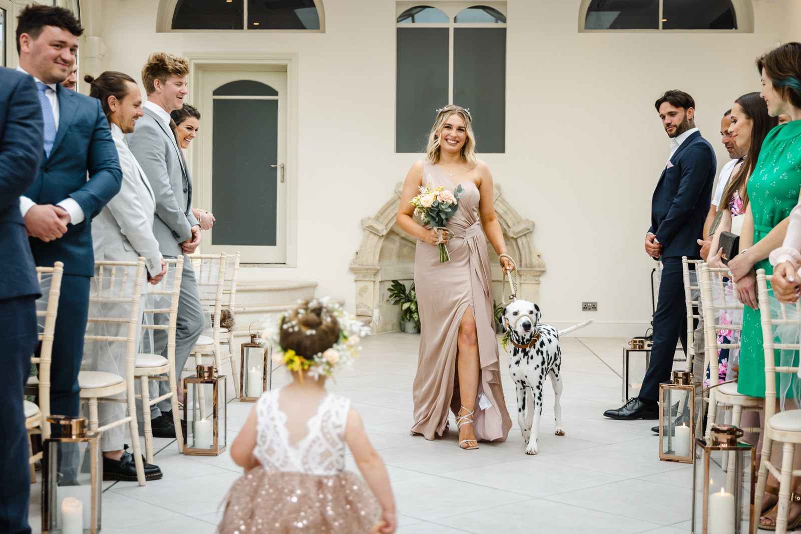 A flower girl walks the aisle toward a bridesmaid holding the Dalmatian