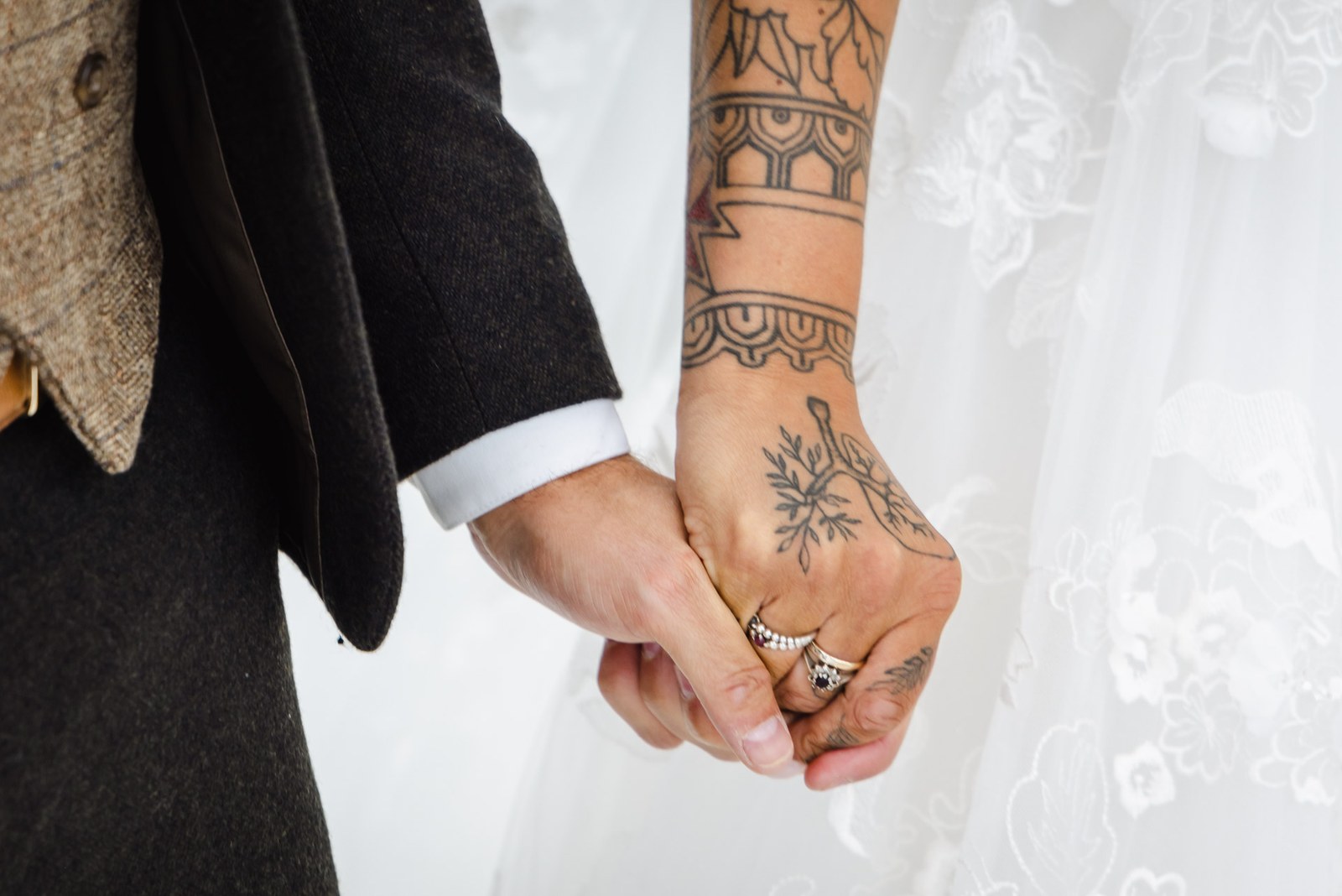 Close-up of the bride's tattooed hand clasped in the groom's during the ceremony