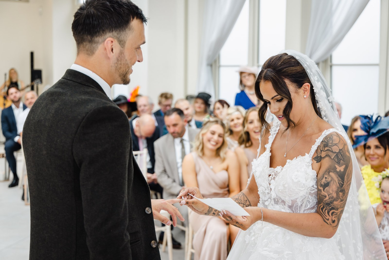 The bride places the ring on the groom's finger as guests look on
