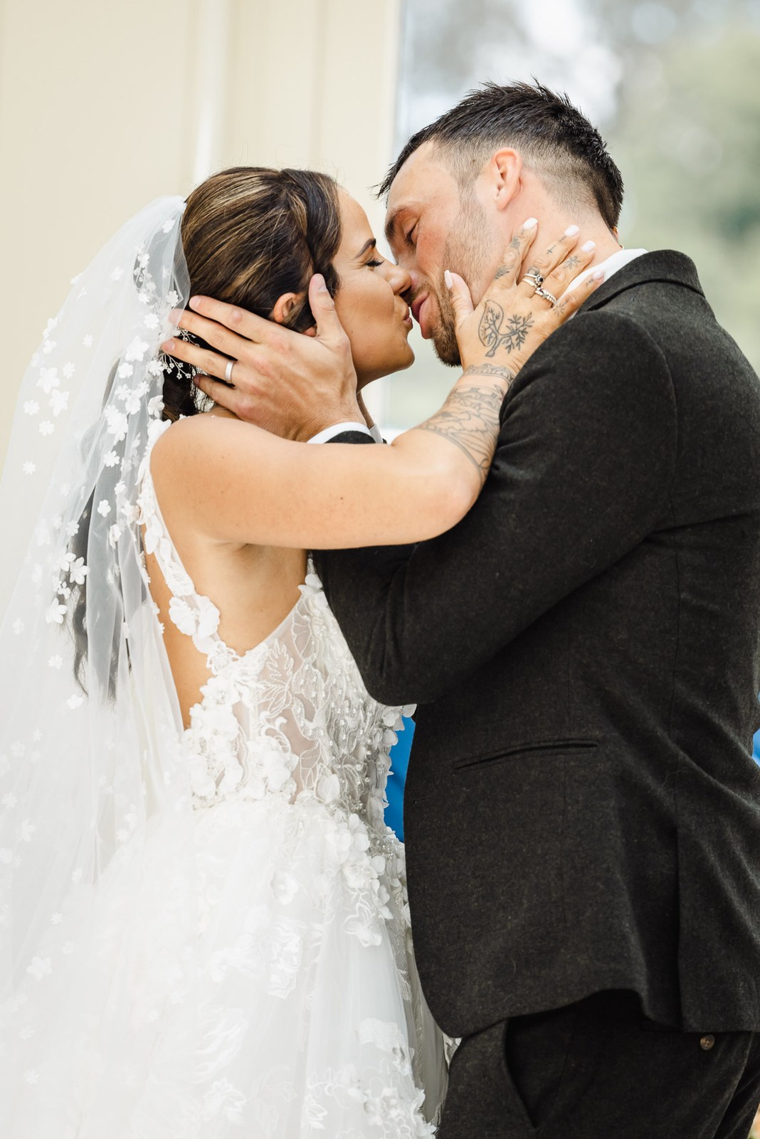 The bride cradles the groom's face as they share their first kiss