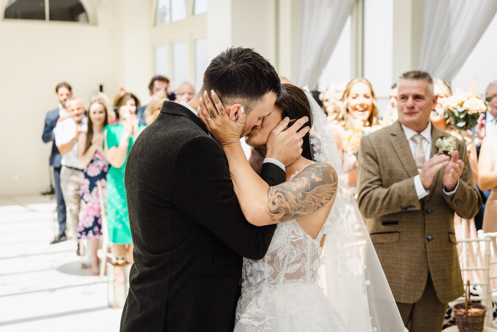 The newlyweds kiss at the aisle's end while the father of the bride applauds