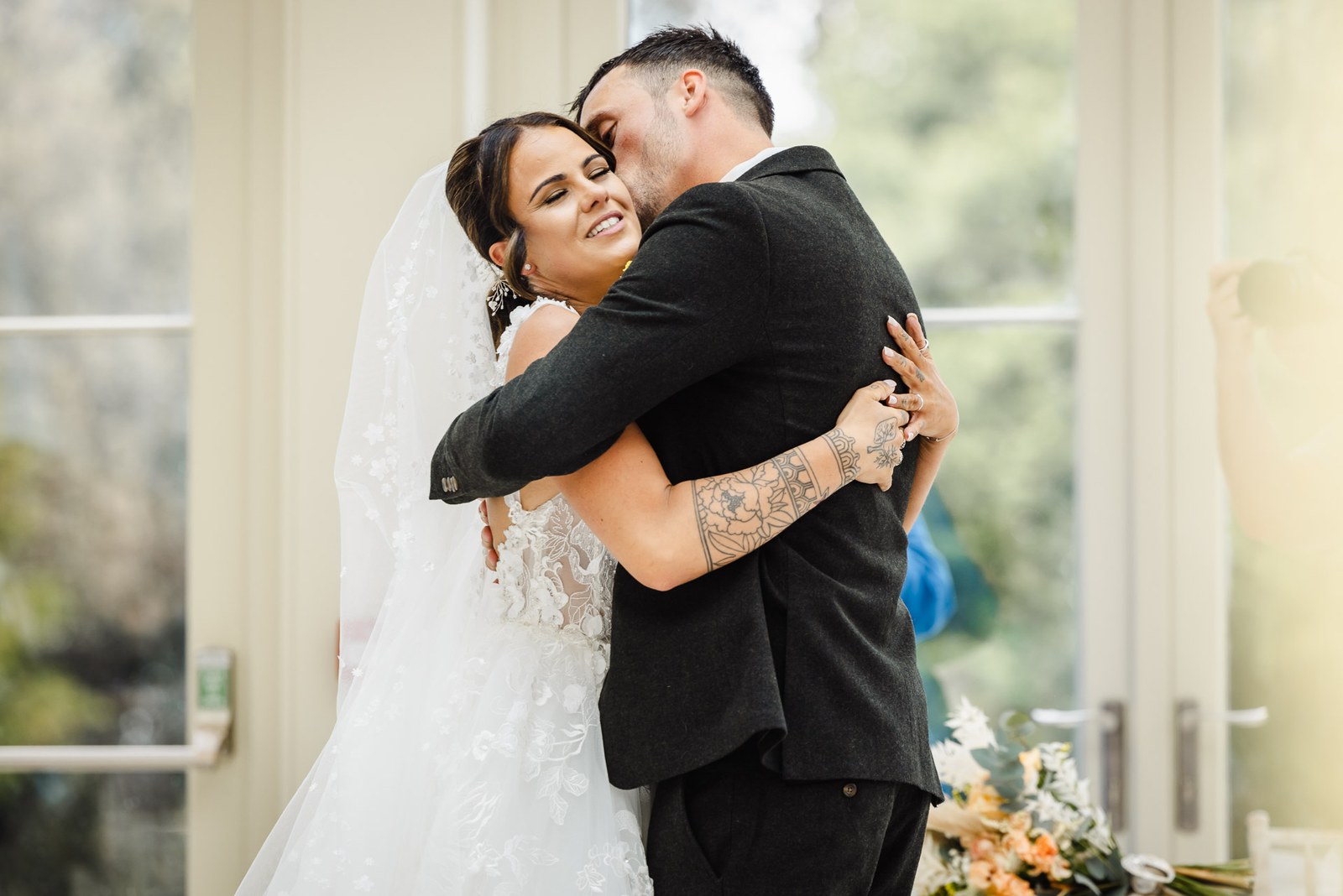 The groom holds the bride close by the tall orangery windows