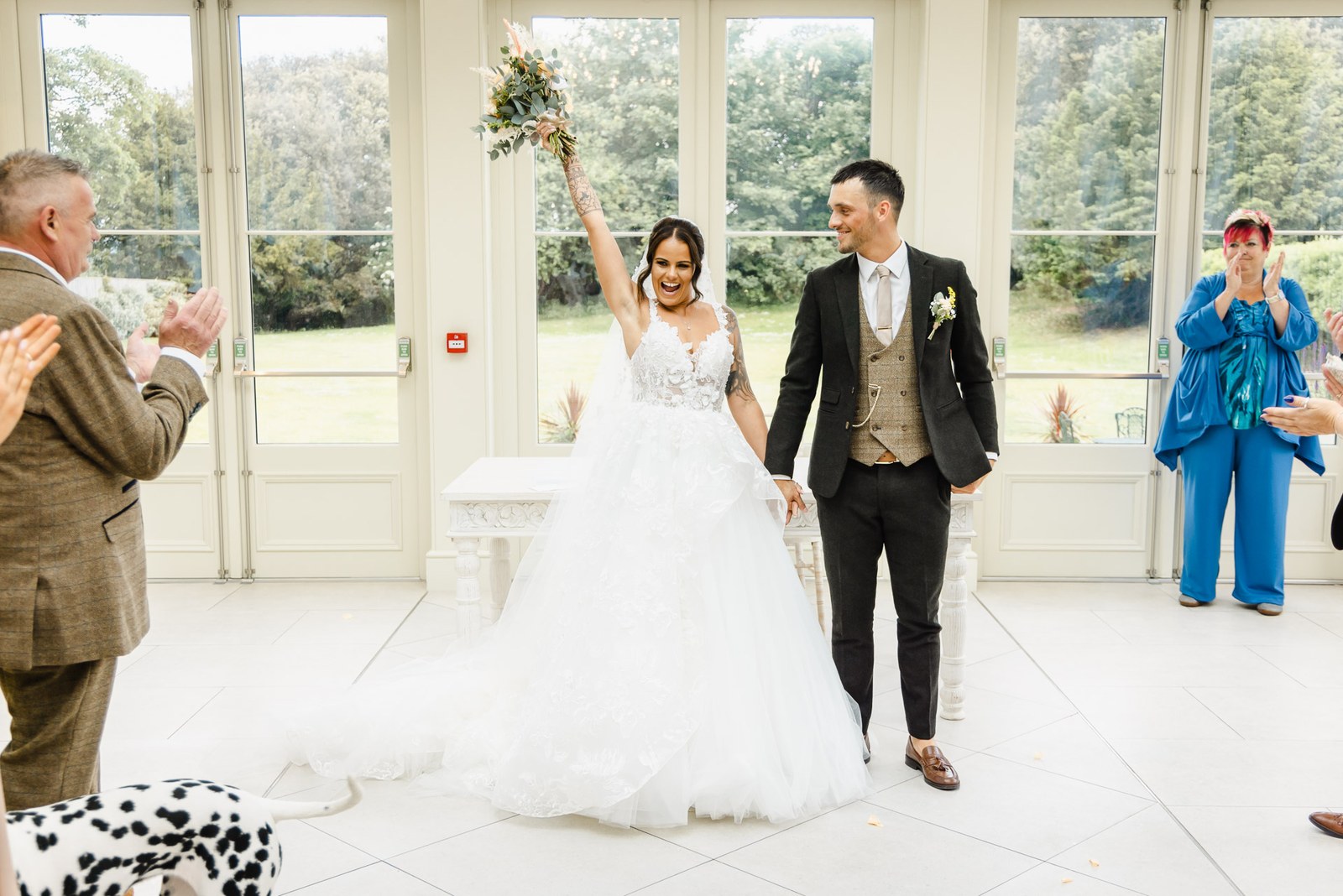 The bride raises her bouquet as the couple walk back through cheering guests