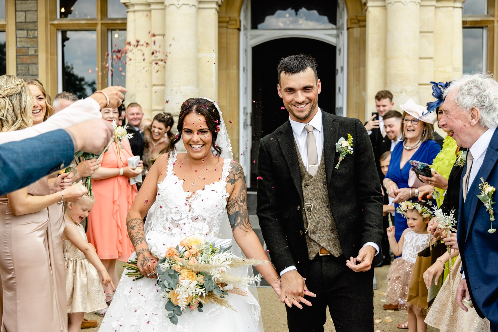 Confetti falls as the couple leave through the stone columns of Clevedon Hall