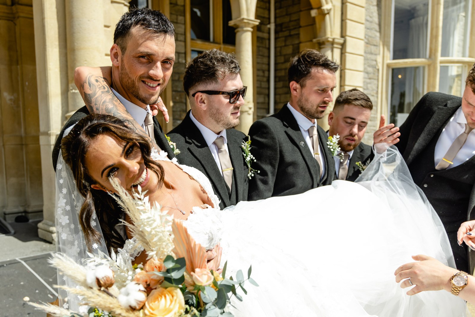 Groomsmen lift and carry the laughing bride outside the venue