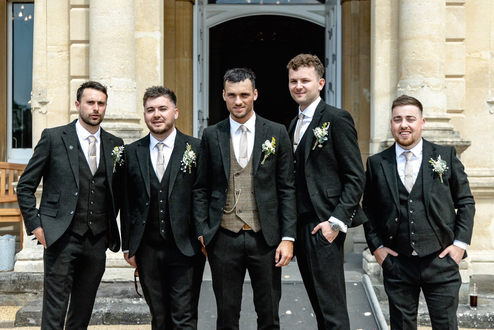 The groom and groomsmen in dark suits on the steps of Clevedon Hall